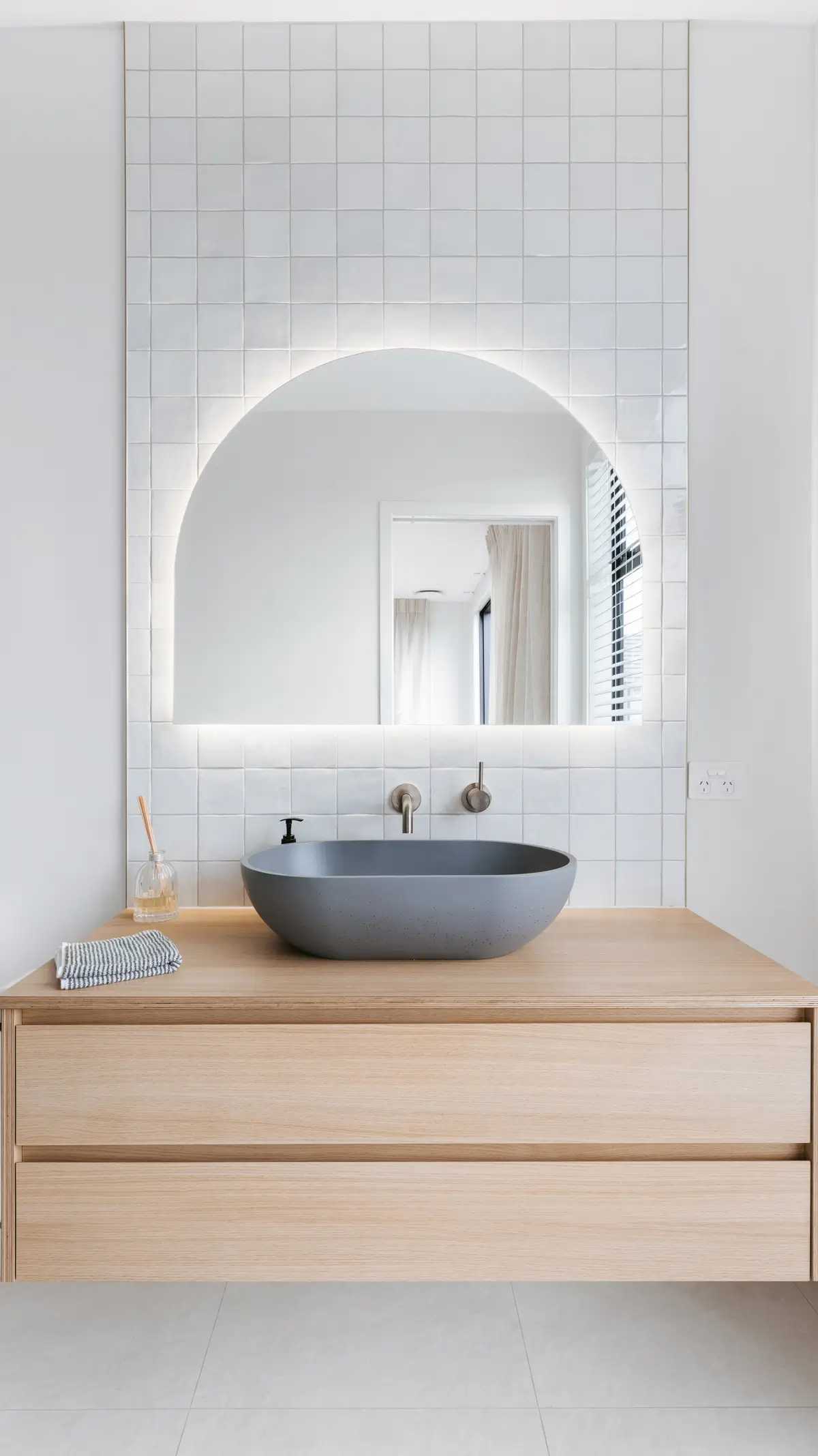 Bathroom design with grey vessel basin, timber vanity and illuminated arched mirror